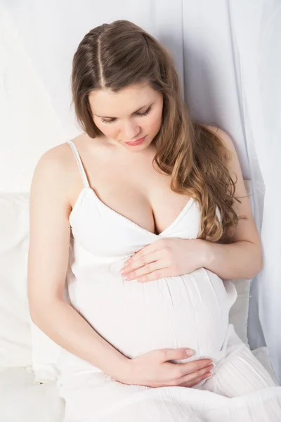 Vackra gravid kvinna i vit klänning nära fönster — Stockfoto