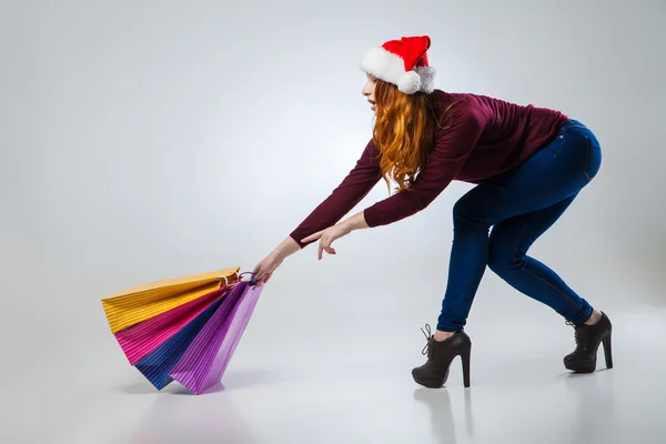 Girl in winter hat with shopping bags over gray — Stock Photo, Image