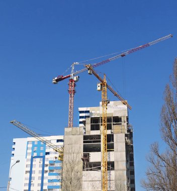 Mavi gökyüzüne karşı yüksek binaların üzerinde inşaat vinçleri