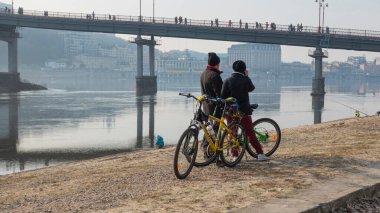 Kiev. Ukrayna. 8 Mart 2017 Bir bahar günü, Dnieper yakınlarında bisiklet süren genç bir çift yaya köprüsünün arka planında
