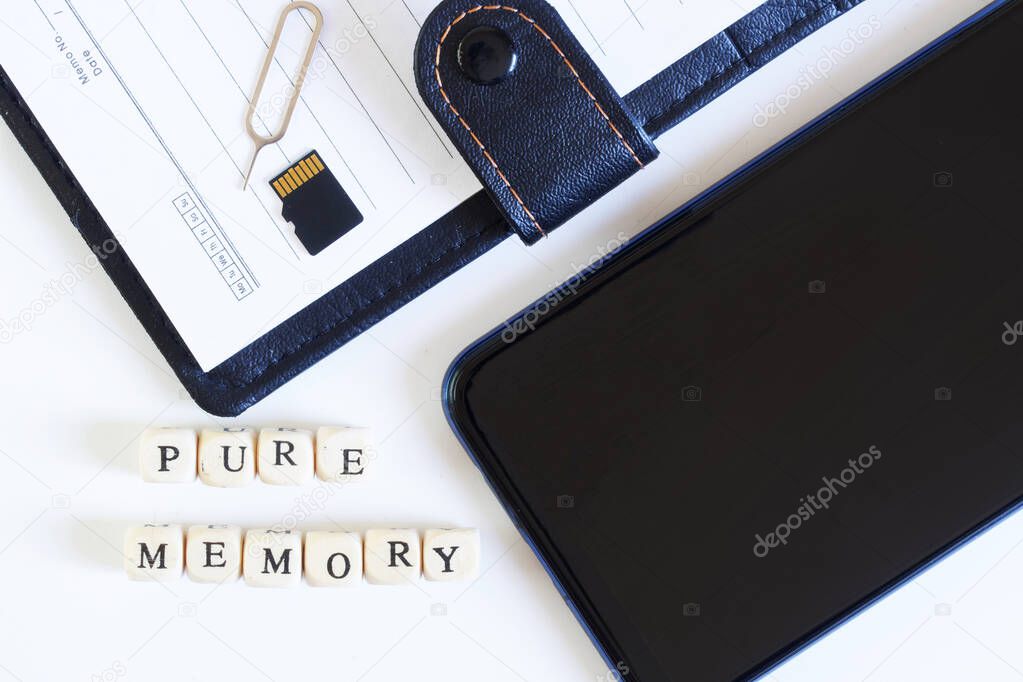 Pure memory lettering next to an open blank notebook, micro-sd memory card, smartphone and ejector for ejecting a SIM card. Digital technologies and human memory. Close-up