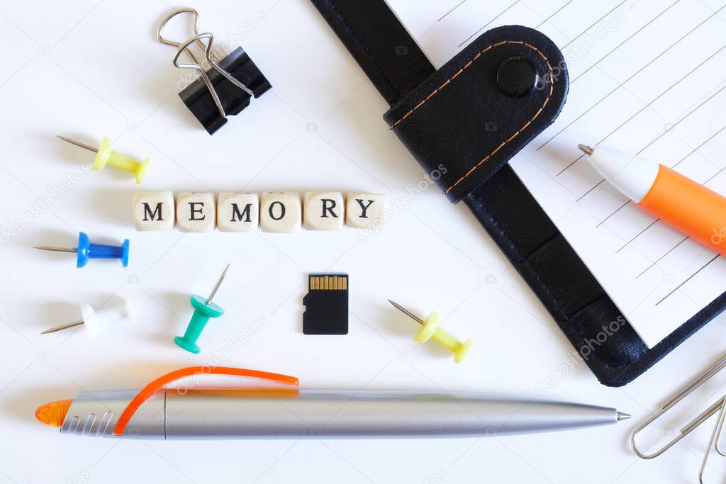 Micro-SD memory card surrounded by items from the office - pens, paper clips, and a notepad, next to the inscription memory. Close-up