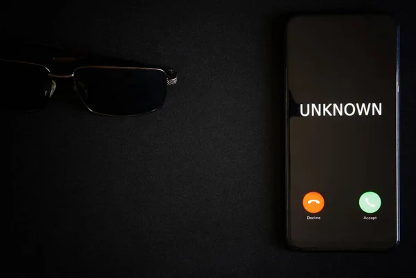 A smartphone with an unknown call lies on a dark surface next to black sunglasses. The problem of anonymity and espionage with modern gadgets. Protection of personal information