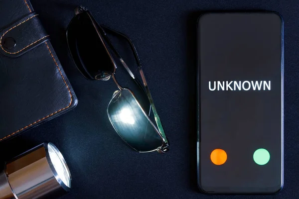 A modern smartphone with an unknown call, sunglasses and a flashlight lie on a black surface. The problems of anonymity and espionage using gadgets. Close-up