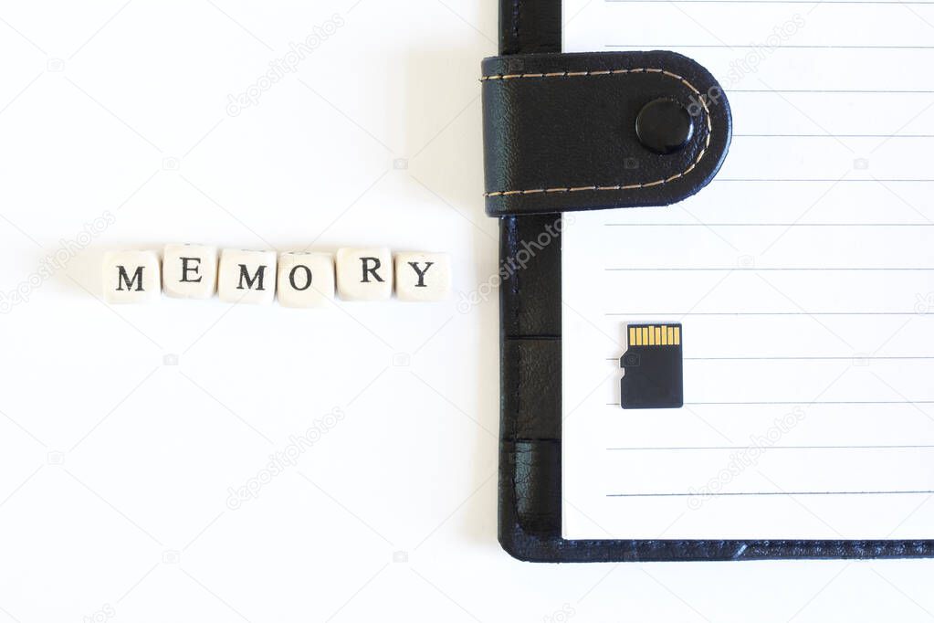Micro SD memory card lies on an open notebook next to the inscription. Old and modern data storage. Miniaturization. White background. Free space for an inscription.