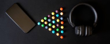 Akıllı telefon, kablosuz kulaklıklar, kulak minderleri ve renkli toplar siyah bir yüzeye uzanır. Kulaklıkla akıllı telefonun bluetooth eşleşmesini taklit et. Yukarıdan görüntüle