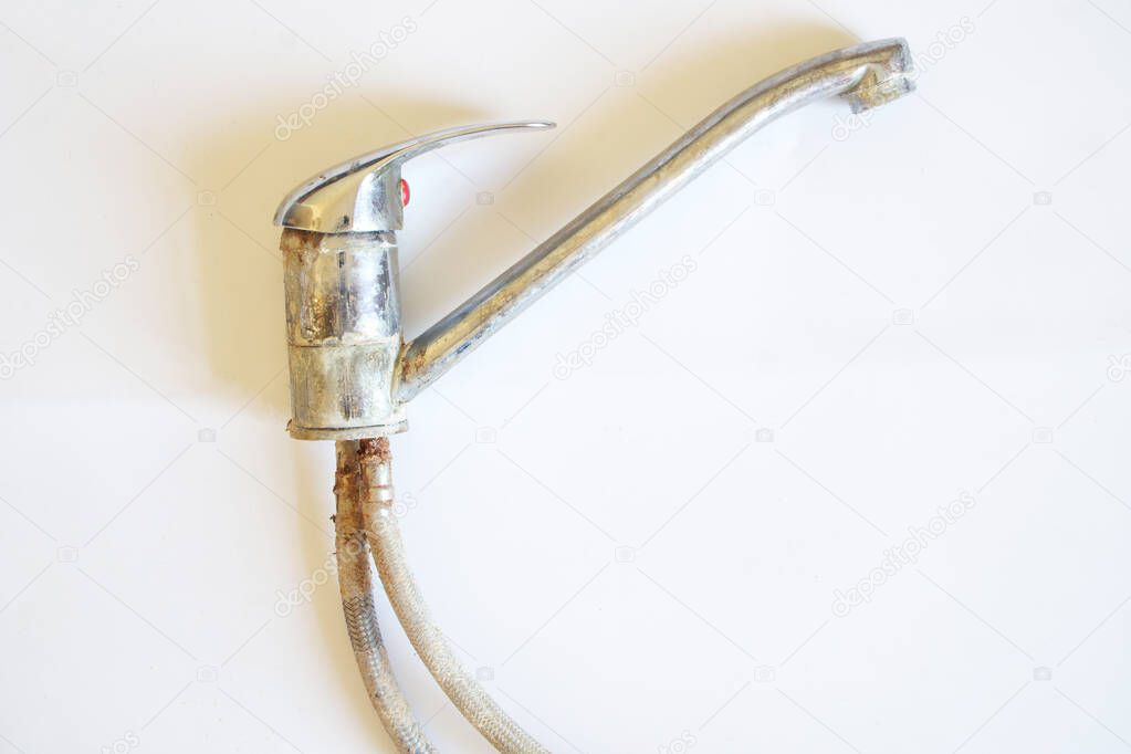 A dismantled, old, lime-coated water tap lies on a white background. Close-up