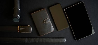 Siyah deri kaplı bir defter, altın renkli tokalı bir kemer, bir akıllı telefon, bir tablet ve karanlık bir yüzeyde bir budayıcı. Erkek eşyası ya da hediye. Erkeklik. Yukarıdan görüntüle
