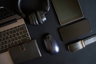 Bir blog yazarının ya da ofis çalışanının iş aksesuarları karanlık arka planda yatar. Laptop, tablet, akıllı telefon, kablosuz kulaklık, bilgisayar faresi, not defteri ve deri kemer. Minimalist siyah tekno trend.