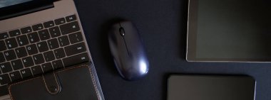 Bir blogcunun ya da programcının iş aksesuarları karanlık arka planda yatar. Laptop, tablet, akıllı telefon, kablosuz kulaklık, bilgisayar faresi ve deri kaplı defter. Siyah tekno trend. Pankart