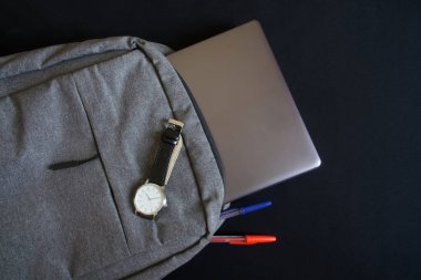 Gri tekstil bir sırt çantasında zarif mekanik saati olan gümüş renkli bir ultraviyole ya da dizüstü bilgisayar. Klasikler ve modernlik. Şehir gezgini, öğrenci ya da programcı için aksesuarlar. Koyu arkaplan