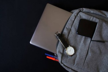 Modern bir tekstil şehrinin sırt çantasında, üzerinde zarif bir mekanik saat bulunan gümüş renkli bir ultraviyole ya da dizüstü bilgisayar ve akıllı telefon bulunur. Klasikler ve modernlik. Karanlık arka plan. Bir yazı için boş alan                     