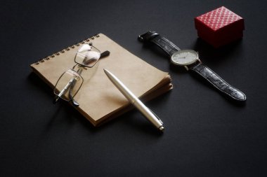 Gözlük, tükenmez kalem, çevre dostu bir defter, bir kol saati ve siyah bir yüzeye uzanan kırmızı bir kutu. Vasiyet yazma ya da dürüst bir mektup yazma kavramı. Eski