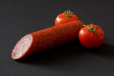 Red tomatoes and sliced salami on a dark background. Anthropomorphism. Metaphor and concept of fertility and male penis. Close-up