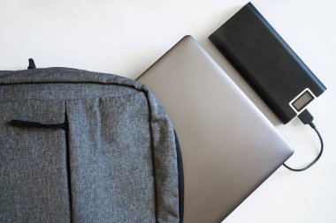 Gri bir tekstil kenti sırt çantası, içinde gümüş bir dizüstü bilgisayar ya da ultraviyole ağ ve beyaz arka planda dış batarya var. Cihazlarla seyahat edip gezmek. Yakın plan. Yukarıdan görüntüle