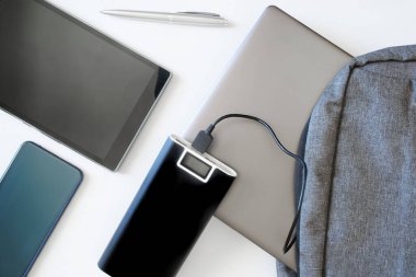 Akıllı telefon, tablet ve harici batarya. Gri tekstil sırt çantasının yanındaki güç bankasında dizüstü bilgisayar ya da ultraviyole var. Beyaz arka plan. Cihazlarla seyahat ya da seyahat konsepti. Yukarıdan görüntüle                       