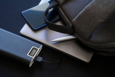 Büyük bir dış batarya - sergilenen güç bankası gri bir tekstil sırt çantası, dizüstü bilgisayar veya ultrabook, akıllı telefon ve tükenmez kalemin yanında duruyor. Cihazlarla seyahat edip gezmek. Yakın plan.