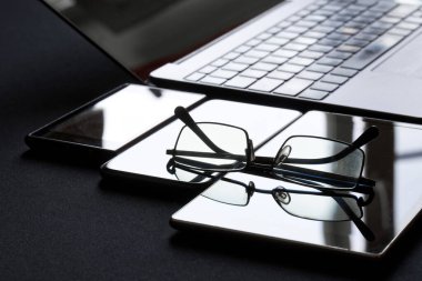 Modaya uygun şeffaf bardaklar çeşitli cihazların yanında bulunur. Defterler, akıllı telefonlar ve tabletler. Cihazlarla çalışmanın insan görüşü üzerindeki olası etkisini düşünün. Yakın plan.