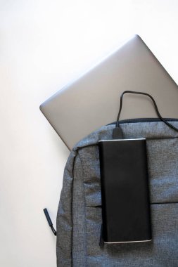 Gümüş dizüstü bilgisayarı olan gri tekstil sırt çantası ya da ultrabook ve beyaz arka planda geniş bir güç bankası. Seyahat ederken ya da seyahat ederken aletleri şarj etme kavramı. Yukarıdan görüntüle