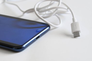 Beyaz imzalı usb tip-c konnektörü mavi bir akıllı telefonun yanında ışık yüzeyinde yatıyor. Cihazları bağlamak ve şarj etmek. Veri iletimi ve modern teknolojiler kavramı. Makro. Seçici odak            
