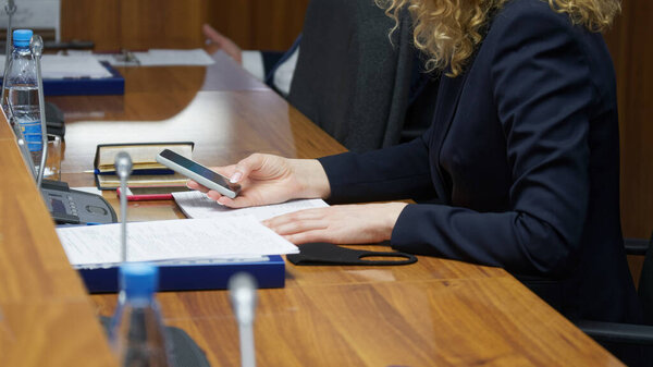 A woman is typing text on a smartphone while sitting at a table in the office. Working with programs and documents. Workspace. No face     