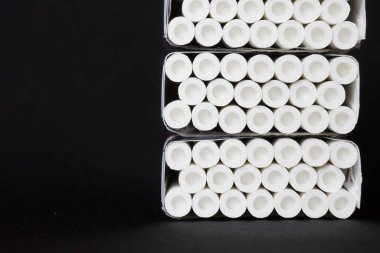 Hava odalarıyla donatılmış beyaz filtreli pek çok sigara koyu arka planda üç paket halinde yatar. Yakın plan. Bir yazı için boş alan