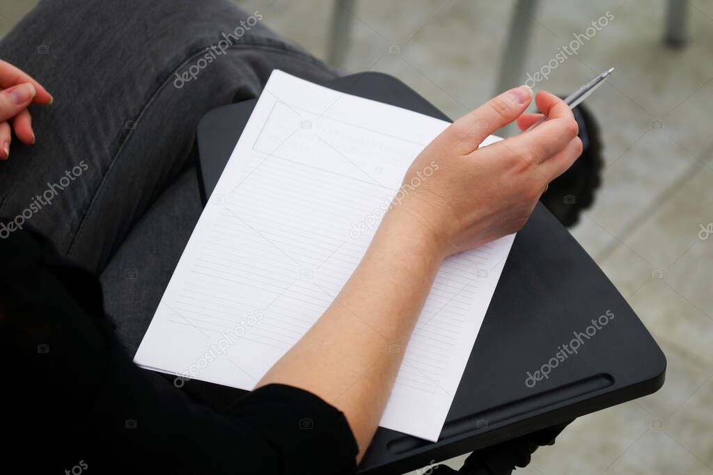A girl is preparing to fill out a blank form, write an essay or dictation, sitting on a school chair with a writing stand. View from above. No face