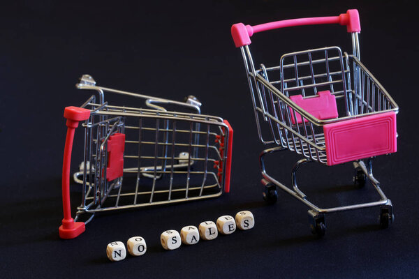 Fallen empty metal supermarket trolleys and no sales lettering on black background. Deficit, economic crisis, inflation and no shopping concept. Close-up