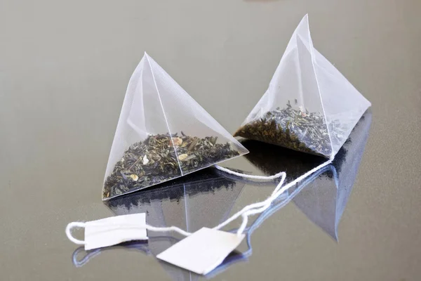 带有绿茶和干果的白色金字塔茶袋盖在反光的背景上 有选择的重点 — 图库照片