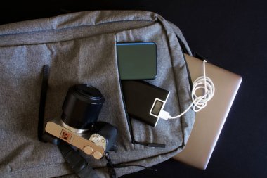 Modern cihazlar - aynasız kamera, dizüstü bilgisayar veya ultrabook, akıllı telefon ve tablet, gri şehir sırt çantasında dış bataryanın yanında yatıyor. Seyahat ederken, seyahat ederken ve öğrenirken cihazları şarj et. Yakın plan.