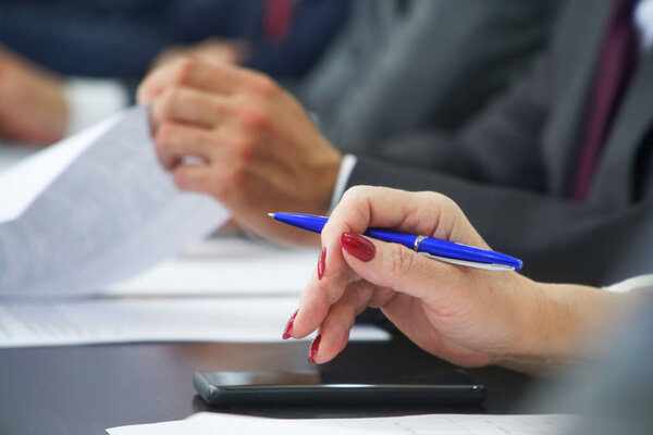 A woman with a fountain pen uses a smartphone during a business meeting or negotiation. Business activity concept using modern gadgets. Without a face