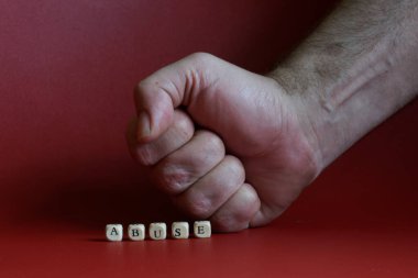 Bir adamın yumruğunun yanındaki yazıyı kötüye kullanma. Aile içi şiddet kavramı. Kırmızı arka plan. Yakın plan.