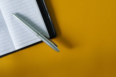 Sarı bir yüzey üzerinde açık bir deri defter ve gümüş bir dolmakalem bulunur. Bir yazı için boş yer. Yakın plan.