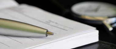 Bir defter ya da günlük, tükenmez kalem ve kol saati siyah bir masanın üzerinde. Anı kitabı, miras ya da günlük rutin planlama kavramı. Web afişi. Seçici odaklanma. Makro