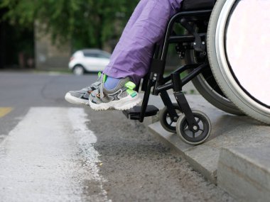A paralyzed girl in a wheelchair prepares to run over the border in front of a pedestrian crossing. Risk of accident and crash. Uncomfortable environment. Close-up. No face