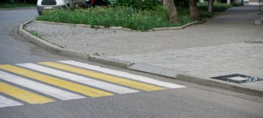 An example of arranging a pedestrian crossing with yellow and white markings and an exit for wheelchairs and people with limited mobility. Accessible urban environment. Daylight