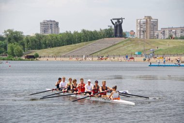 Ural Nehri 'nin yüzeyinde sekiz kürekçiyle birlikte kano, şehir plajı ve Tyl Front anıtı yakınlarında. Hafta sonları kasaba halkının geri kalanı. 10 Temmuz 2021, Rusya, Magnitogorsk. Etkin yaşam biçimi