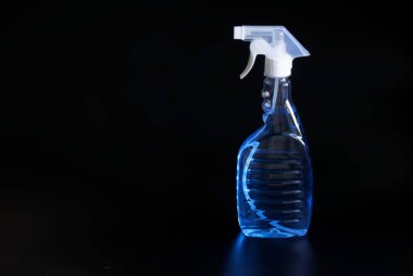 Üzerinde sprey şişesi ve açık mavi dezenfektan olan şeffaf konteynır siyah arka planda duruyor. Mikroplardan, virüslerden ve dezenfeksiyondan temizleme kavramı. Yakın plan.