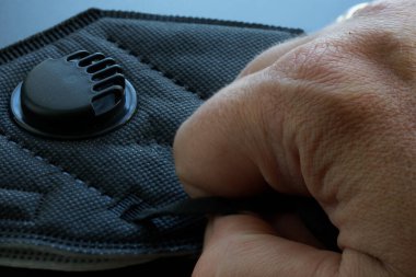 Bir adamın eli siyah bir tıbbi solunum cihazını filtre ve vanayla tutuyor. Solunum cihazı koruma sınıfı KN95, Amerikan N95 ve Avrupa FFP2 ile uyumlu. Yakın plan.