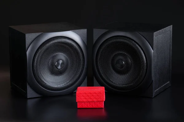 Red gift box and two single-way audio speakers on a black background. Hi-end analog acoustics of a studio, music center or home theater. Musical gift concept. Close-up
