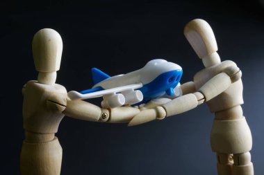 İki antropomorfik model bir oyuncak uçağı dikkatle tutuyor. Hava taşımacılığı ve yolcu uçağı güvenliği kavramı. Siyah arka plan. Yakın plan.