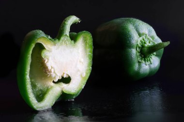 Nem damlalarıyla kaplı, siyah arka planda yeşil dolmalık biberler. Yakın plan.