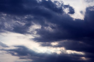 Karanlık gökyüzünde, güneş ışınlarıyla çarpıcı fırtına bulutları.