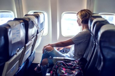 Yolcu uçağın camına bakıyor, uçakla seyahat ediyor, kadın turist uçakta oturuyor. Seyahat kavramı