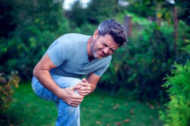 İnsanlar, sağlık ve sorun konsepti - bacaklarında ya da dizlerinde ağrıdan muzdarip mutsuz bir adama yakın durmak
