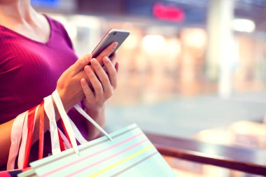 Alışveriş merkezinde cep telefonu ve alışveriş torbaları olan bir bayan müşteri.