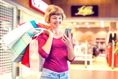 Alışveriş merkezinde cep telefonu ve alışveriş torbaları olan kadın müşteri.