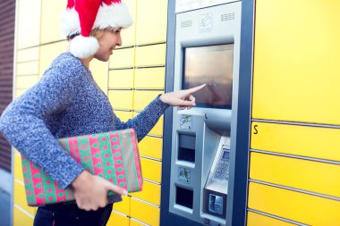 Noel Baba şapkalı kadın paketi depolamak için otomatik self servis terminali ya da dolap kullanıyor.