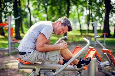 Spor ve parkta egzersiz yaparken dizinde ağrı hisseden mutsuz bir adam. Spor, tıp ve insan konsepti