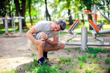 Spor ve parkta egzersiz yaparken dizinde ağrı hisseden mutsuz bir adam. Spor, tıp ve insan konsepti